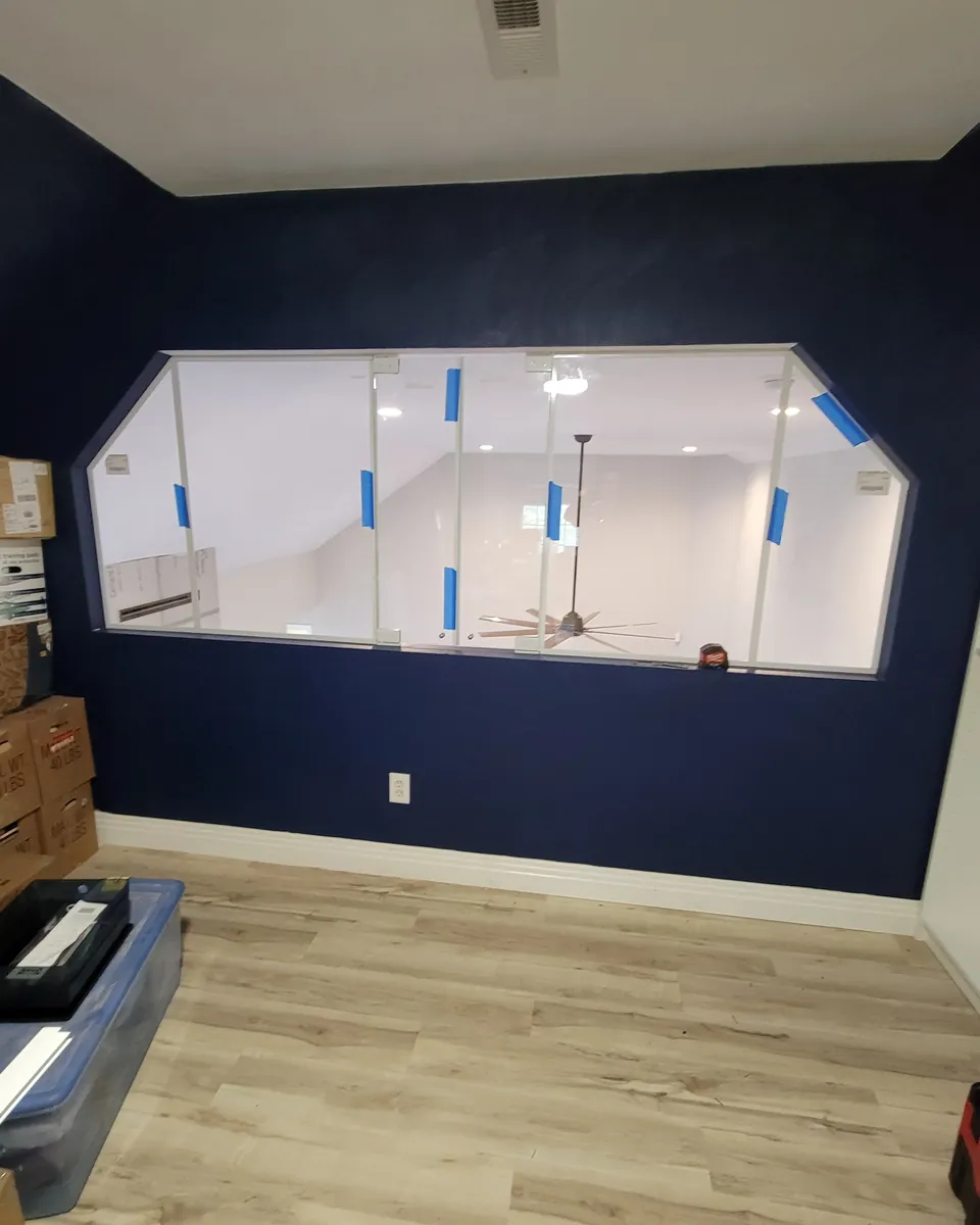 An interior glass window set into a navy wall, blue tape still on the glass during the install