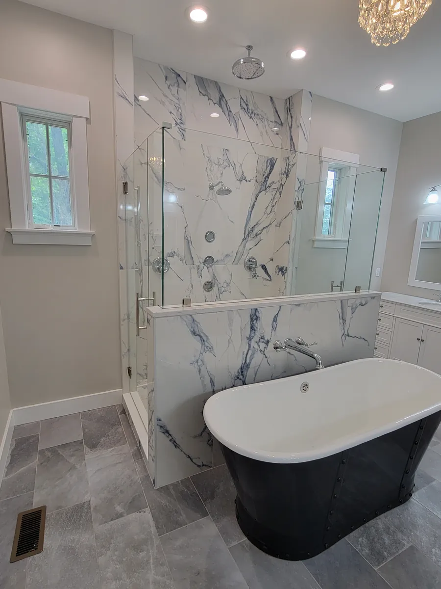 A frameless glass panel on a marble half wall, a black freestanding tub in front of it