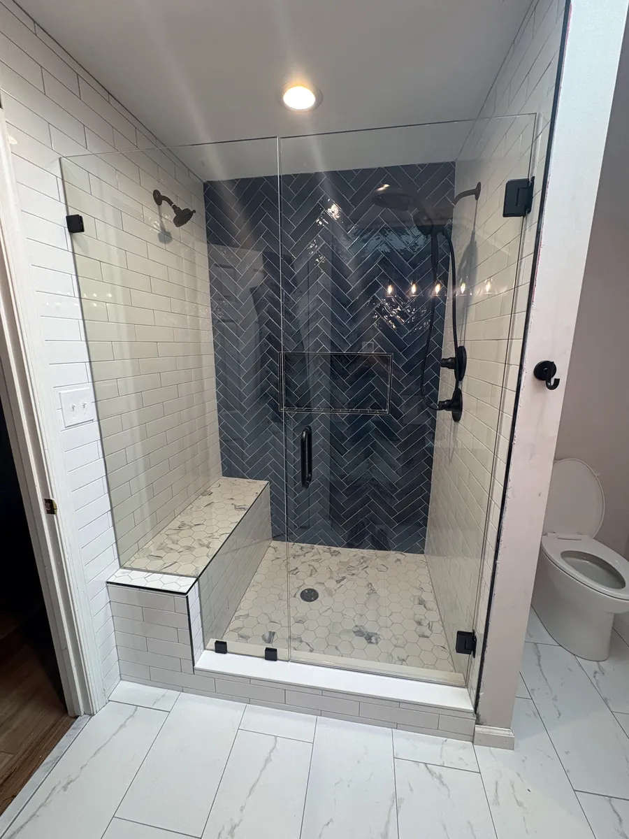 A frameless glass door and panel on a shower with navy herringbone tile and a tiled bench