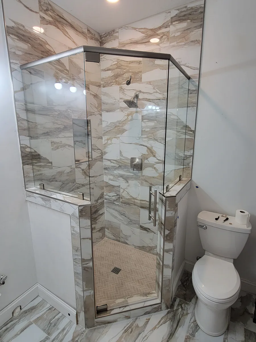 A neo-angle frameless shower with marble-look tile and chrome hardware