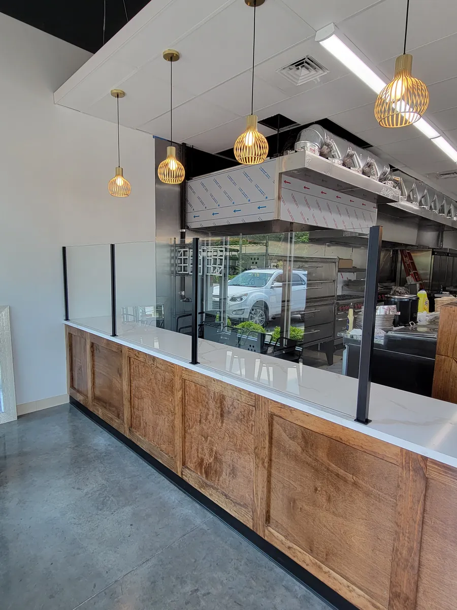 Glass panels on black posts along a wooden counter, a work area behind them